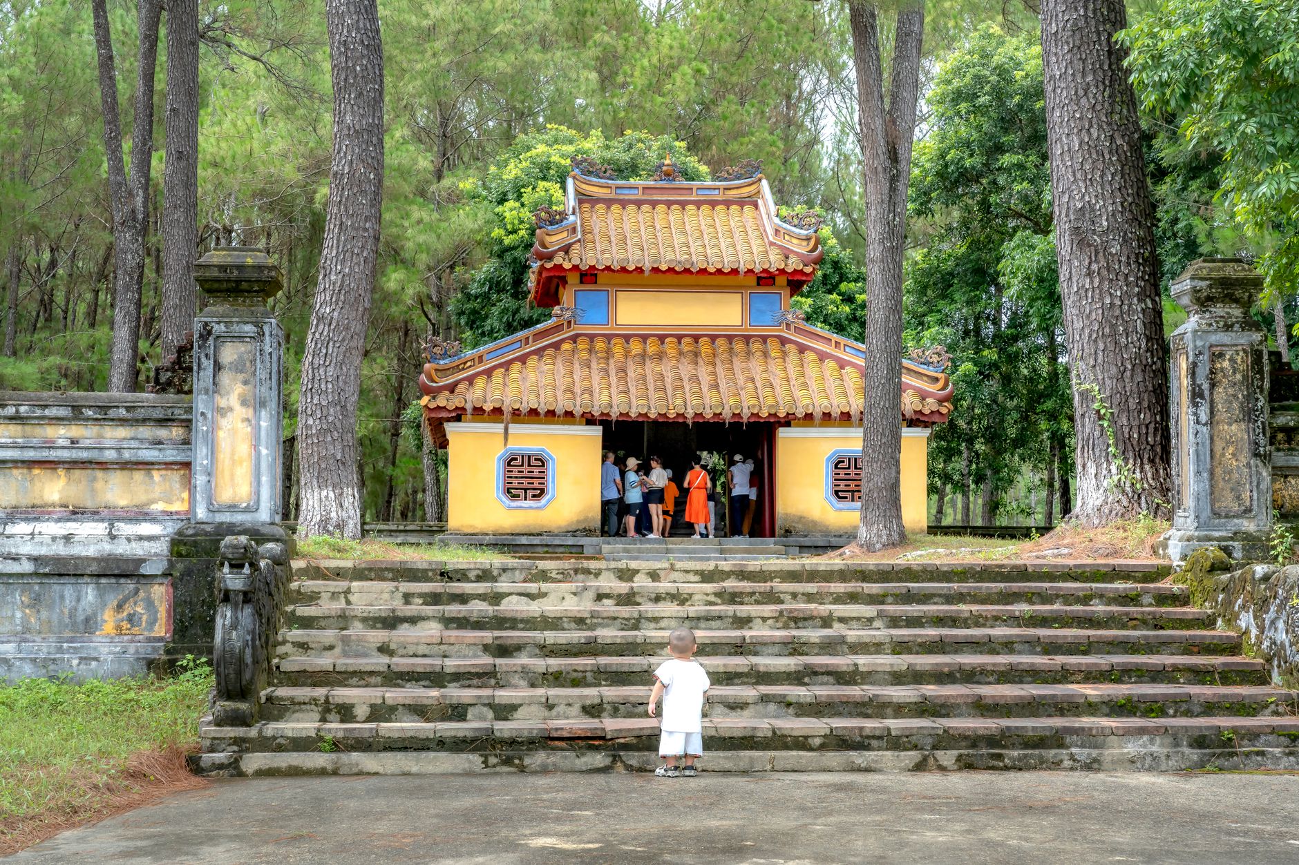 A young child stands before an ancient temple surrounded by lush greenery, exploring the historic site.