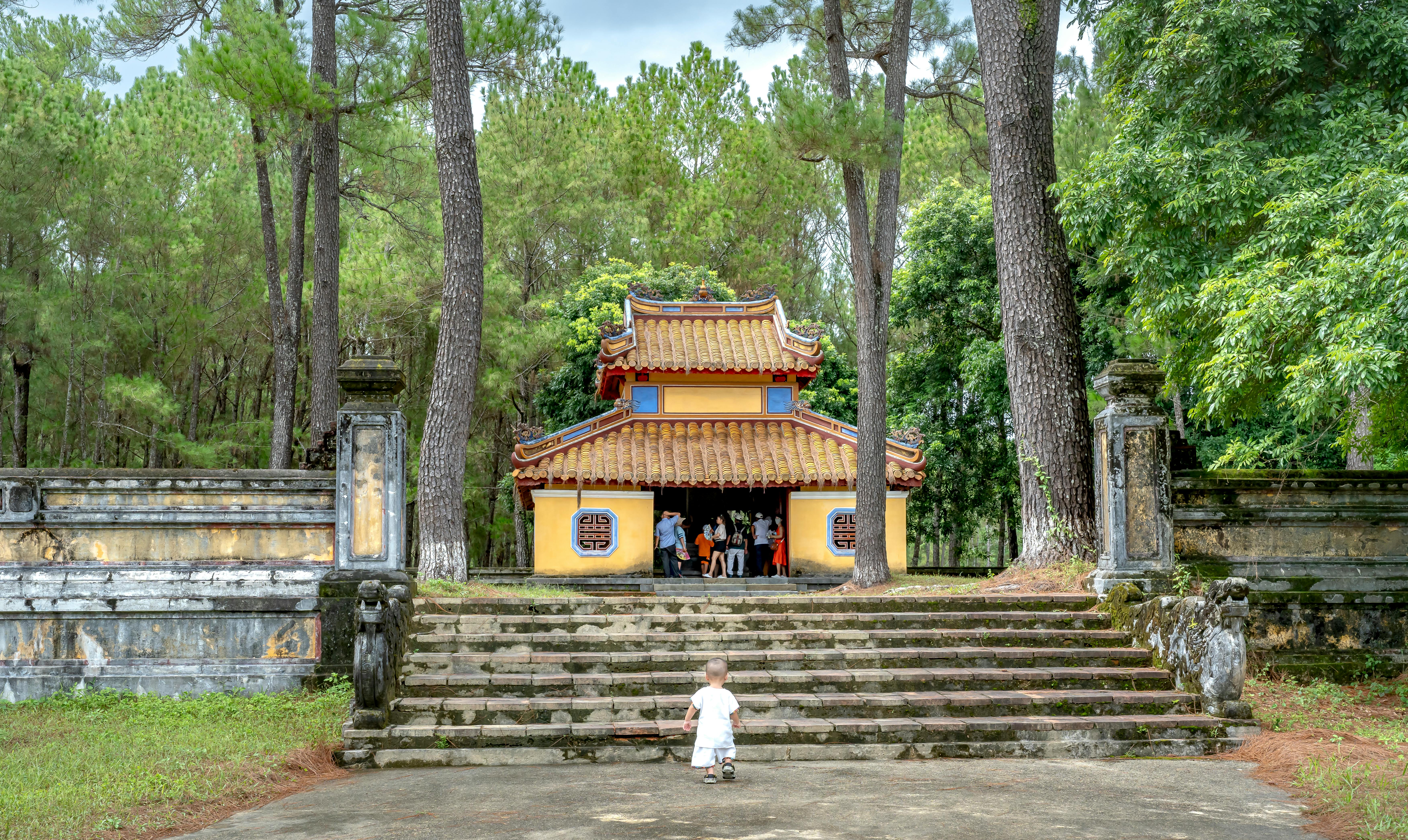 A temple surrounded by trees with stone steps and a child approaching.