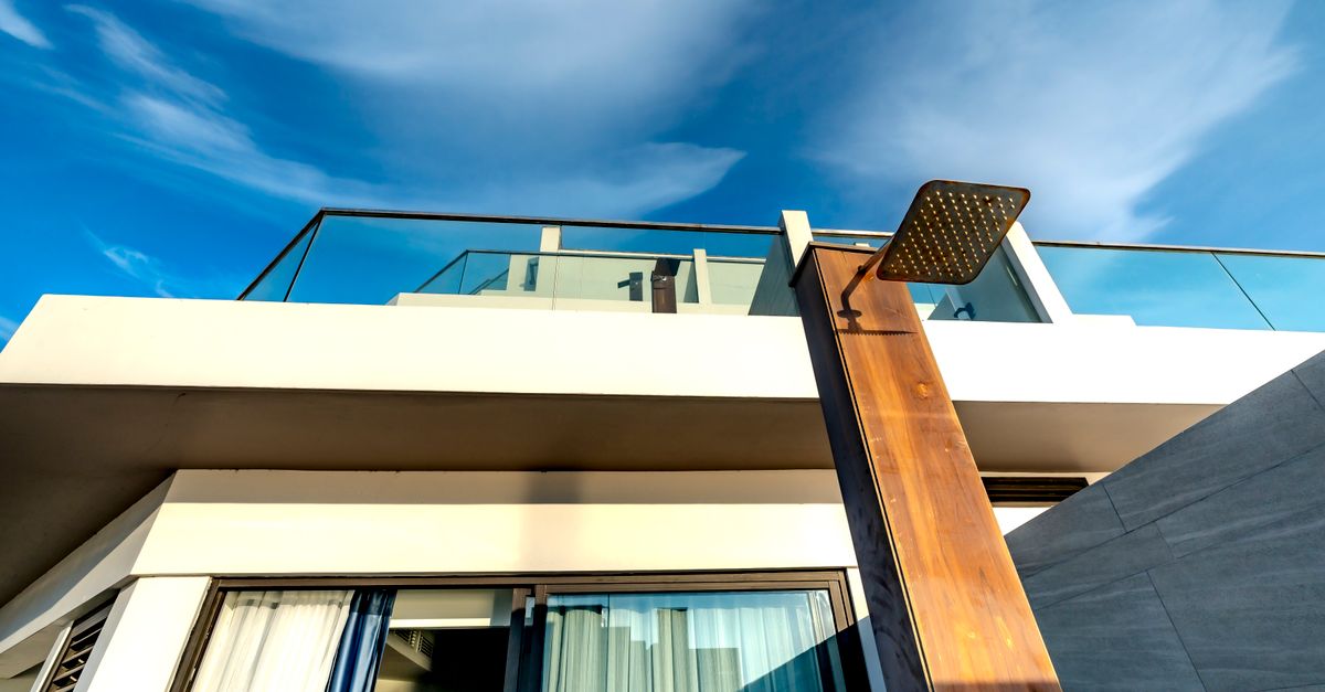 Contemporary terrace design with glass railings and outdoor shower against a vivid sky.