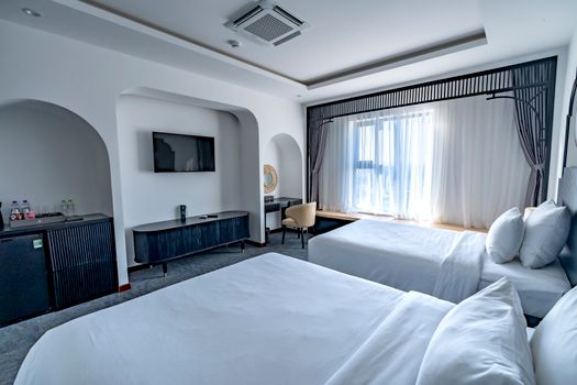 Spacious modern hotel room featuring two beds, a TV, and ample natural light through sheer curtains.