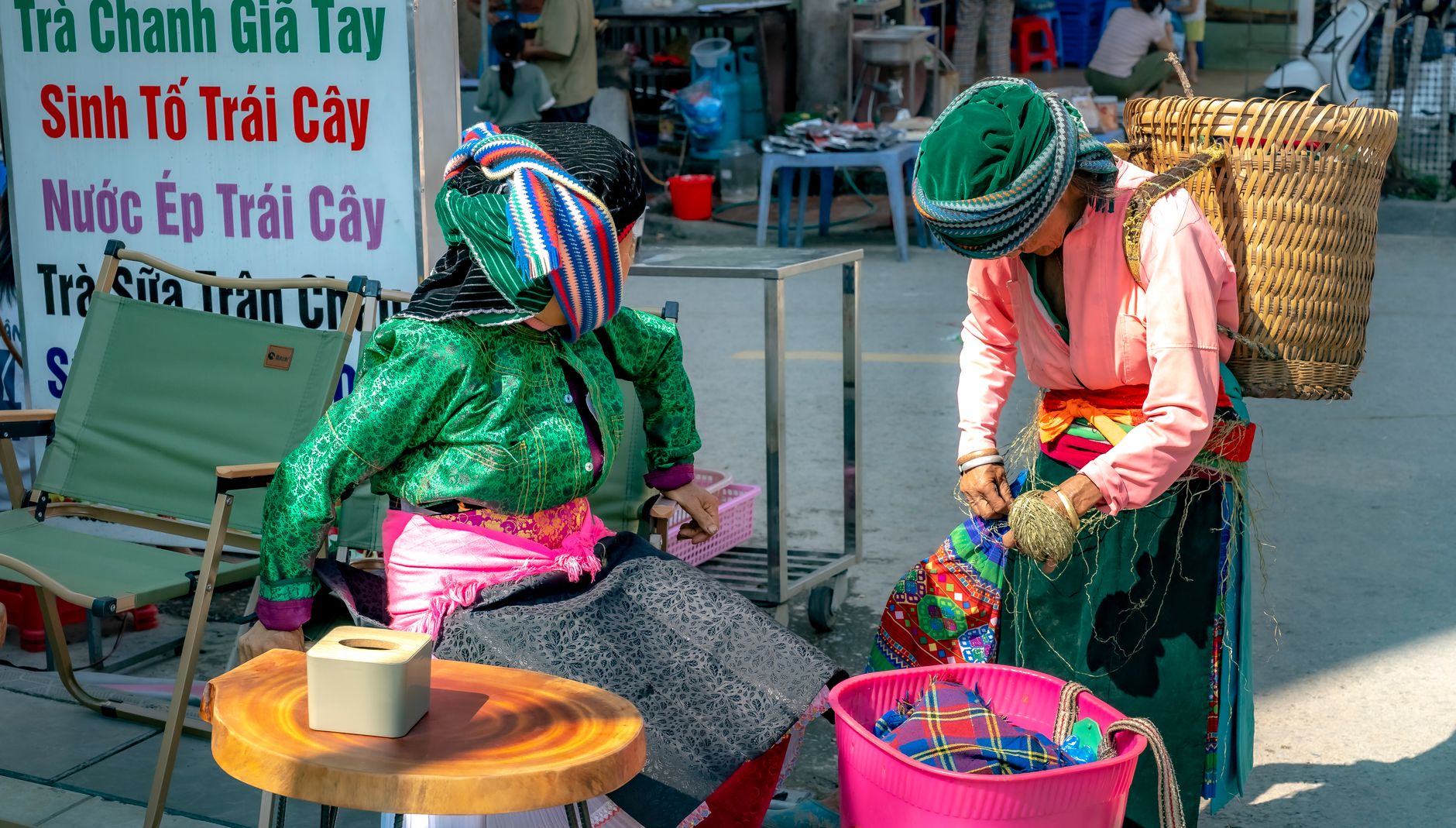 Hmong women in colorful dresses at a bustling Vietnamese street market.