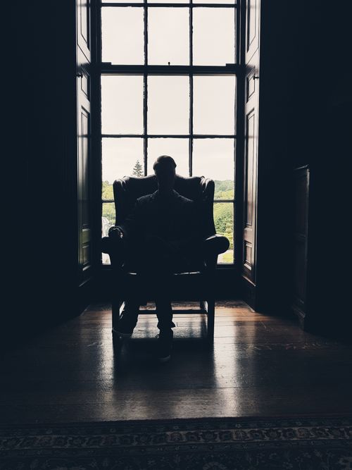 Free A silhouette of a man sitting in a chair, highlighting contrast against a window. Stock Photo