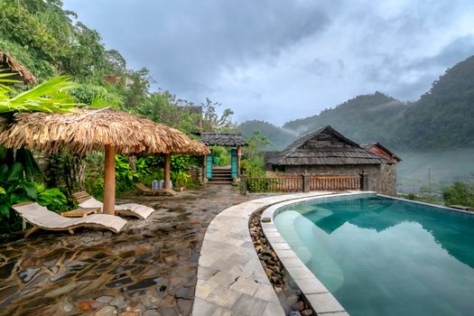 Serene tropical resort with poolside view amidst lush greenery and mountain backdrop.