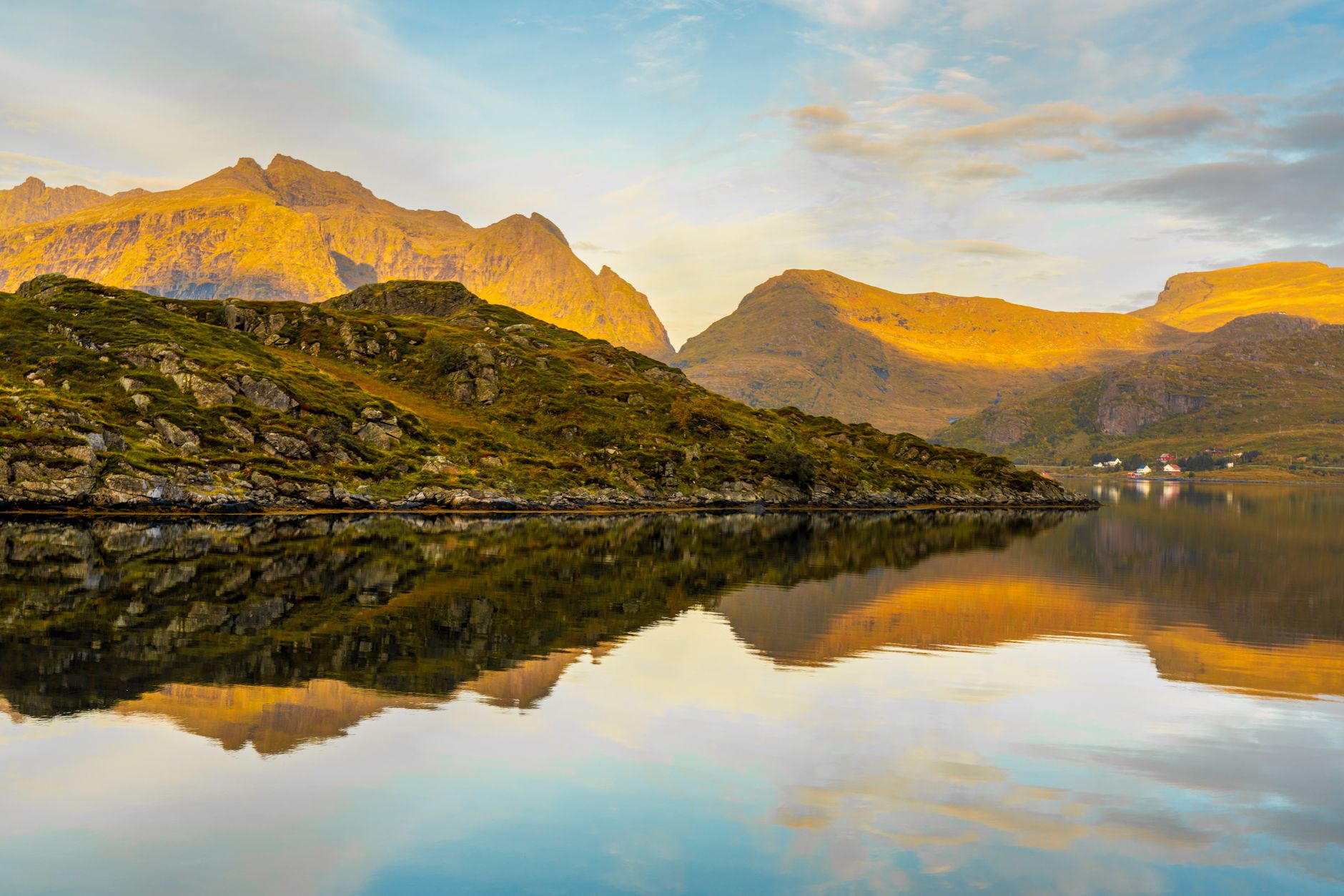 Serene autumn view of Lofoten mountains reflected in calm sea waters under a golden sky.