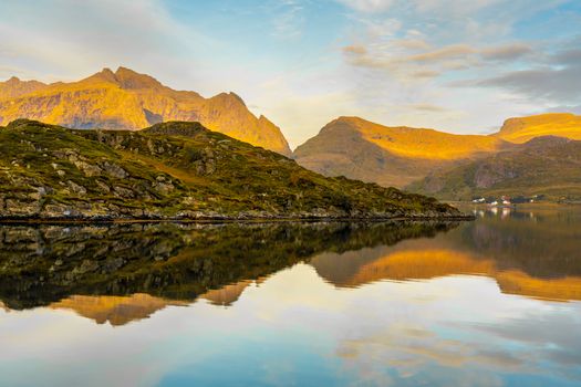 Serene autumn view of Lofoten mountains reflected in calm sea waters under a golden sky.
