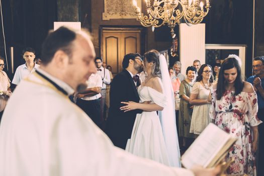 Bride and groom share a kiss during wedding ceremony in an elegant church setting as guests watch with joy.
