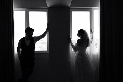Free Black and white silhouette of a bride and groom by a window, creating a timeless and elegant look. Stock Photo