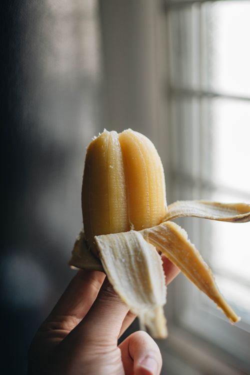 Free Hand holding a peeled banana near a window with natural light streaming in. Stock Photo