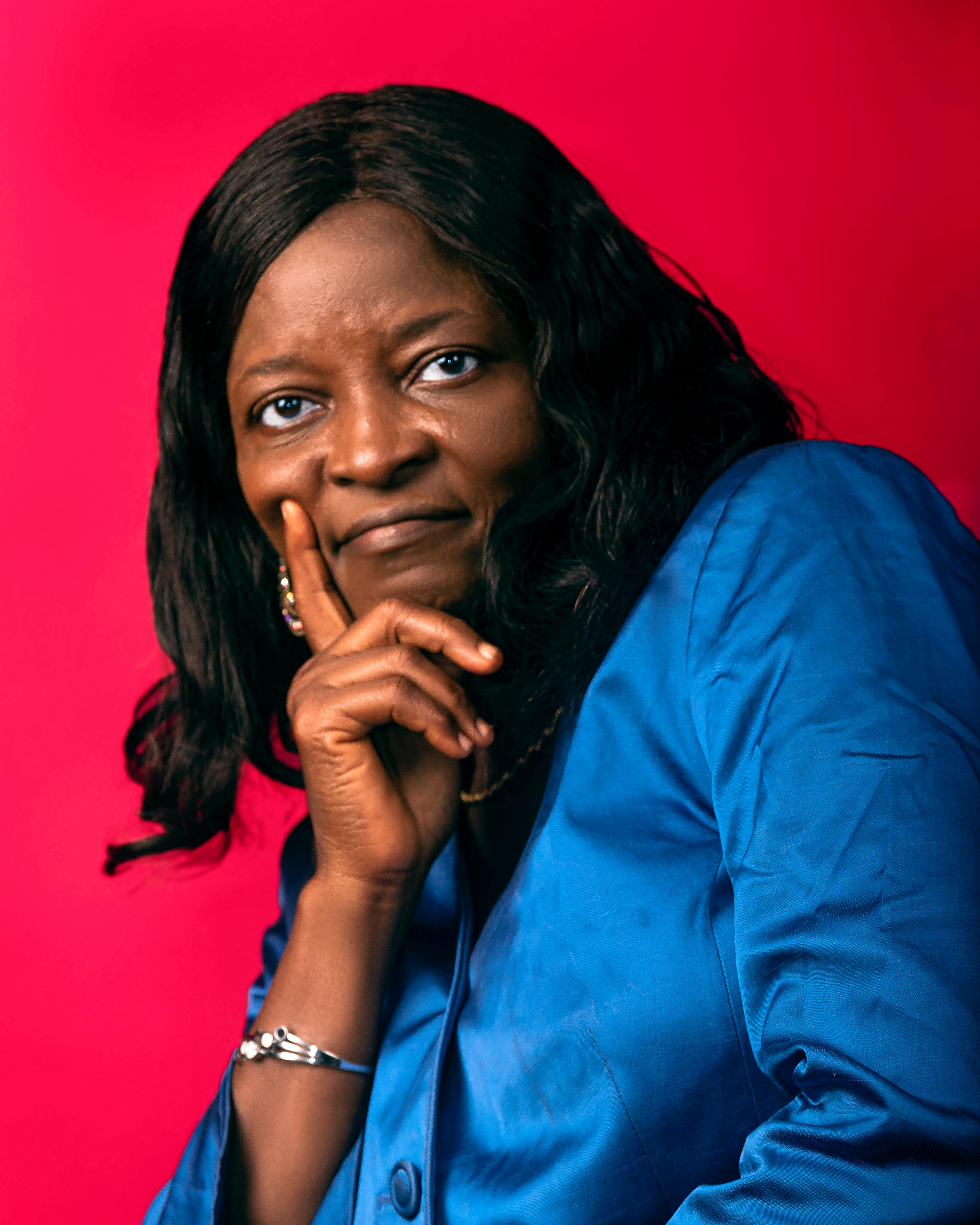 Portrait of a confident woman in a blue suit posing with a thoughtful expression against a vibrant red background.