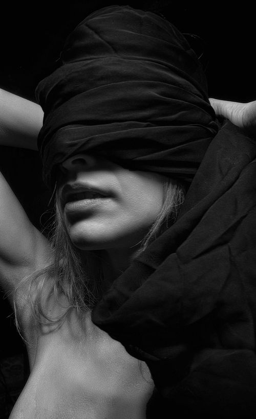 Free A moody black and white portrait of a woman blindfolded with a cloth, evoking mystery. Stock Photo