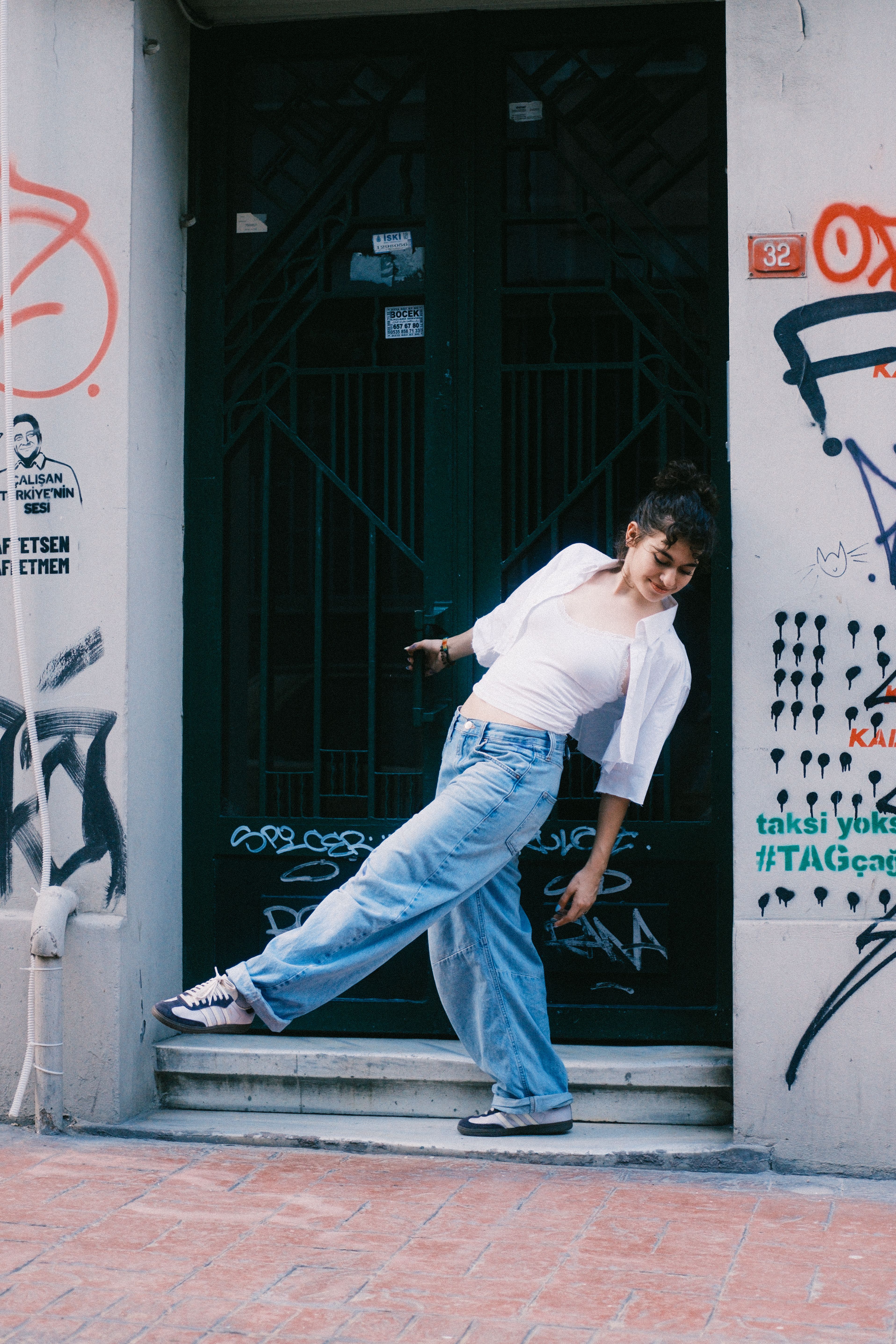 Stylish young woman in casual jeans and sneakers poses in front of a graffiti-covered wall in Istanbul.