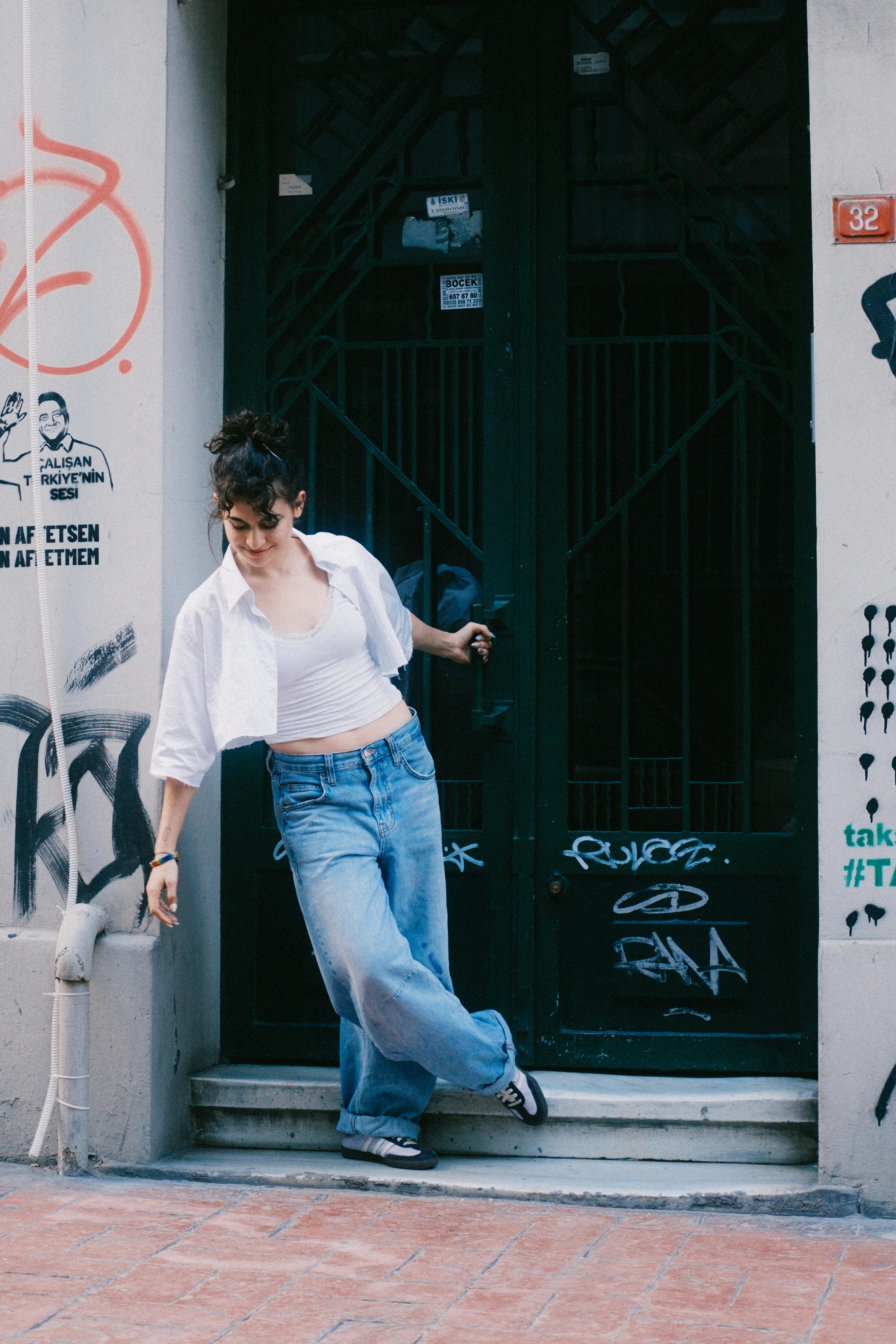 Casual young woman in jeans posed by a graffiti-covered doorway.