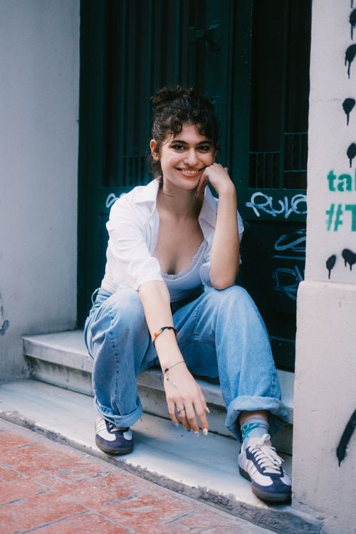 Free A young woman smiles while sitting casually on outdoor steps in an urban setting. Stock Photo