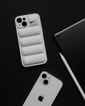 A stylish flat lay of iPhone, case, and tablet in black and white tones.
