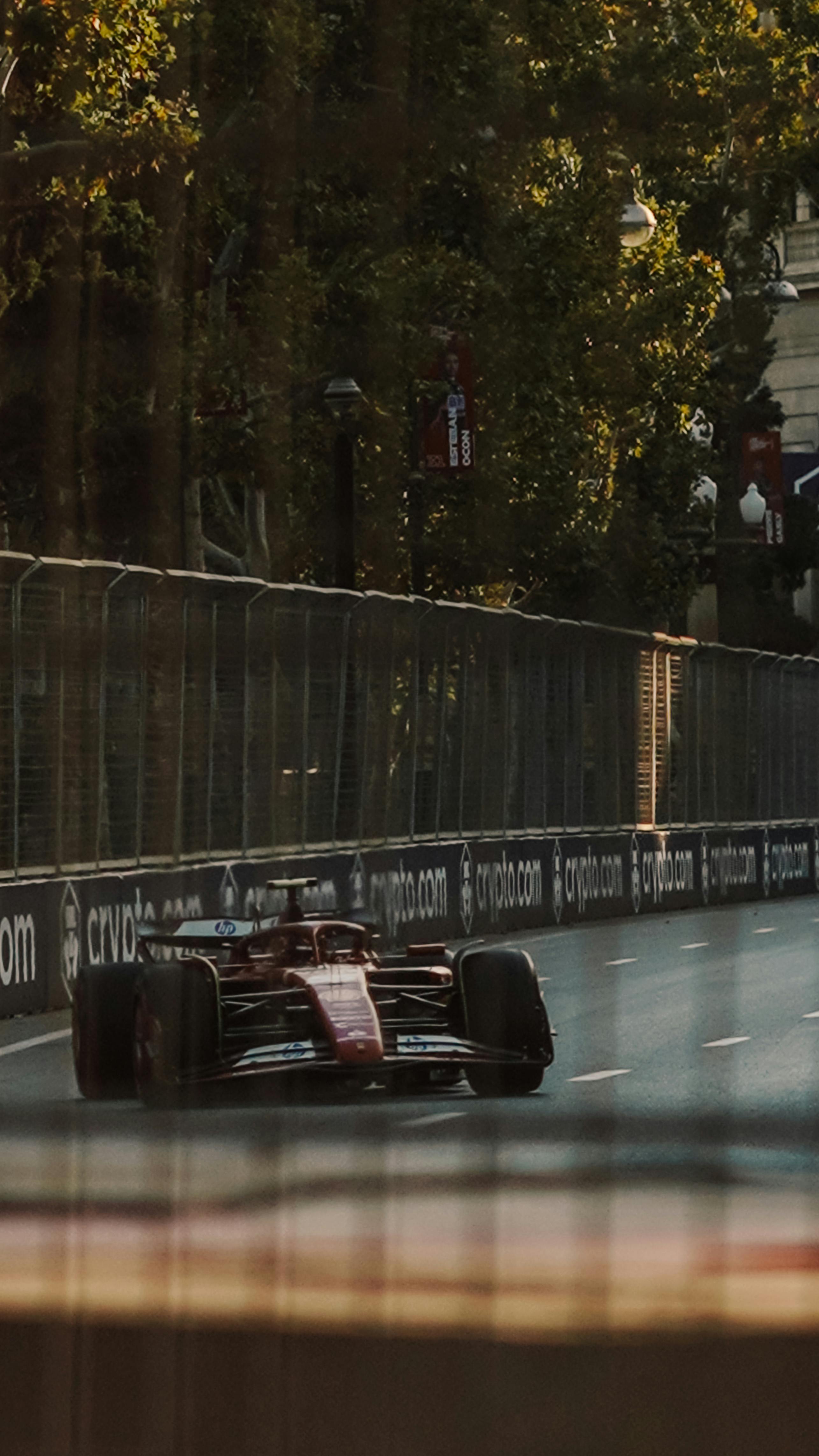 Formula 1 race car speeds through a scenic urban track surrounded by trees and buildings.