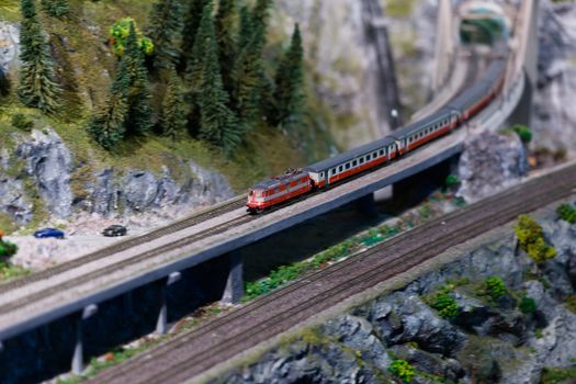 A detailed model train crossing a bridge in a miniature mountainous landscape.