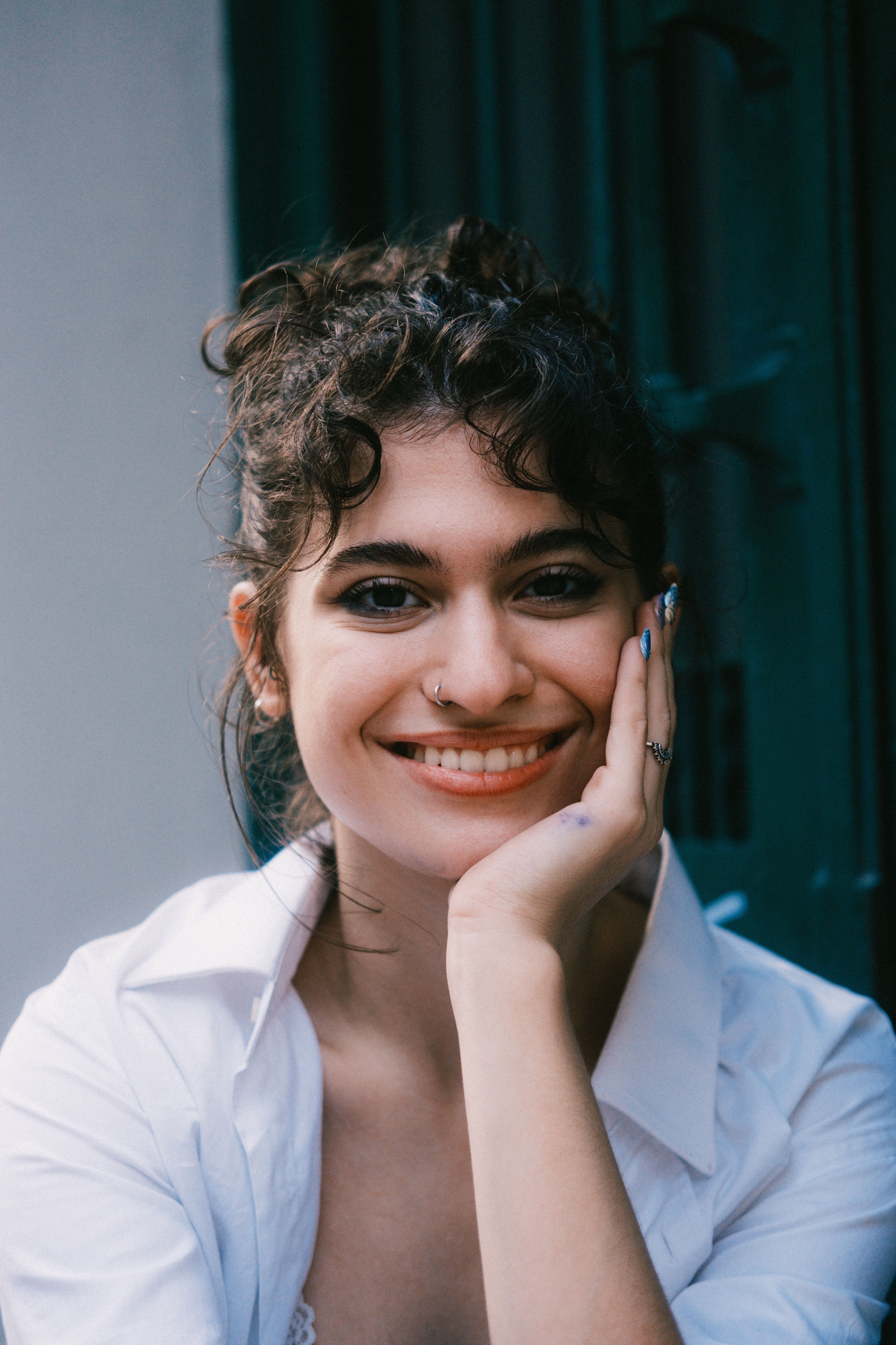 Young woman with curly hair smiling, wearing a white shirt outdoors.