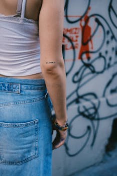 Back view of young woman with a tattoo standing in a graffiti-covered alley.