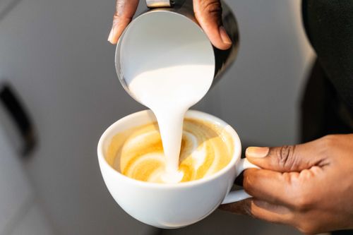 Free Close-up of a barista pouring steamed milk into a coffee cup to create latte art. Stock Photo
