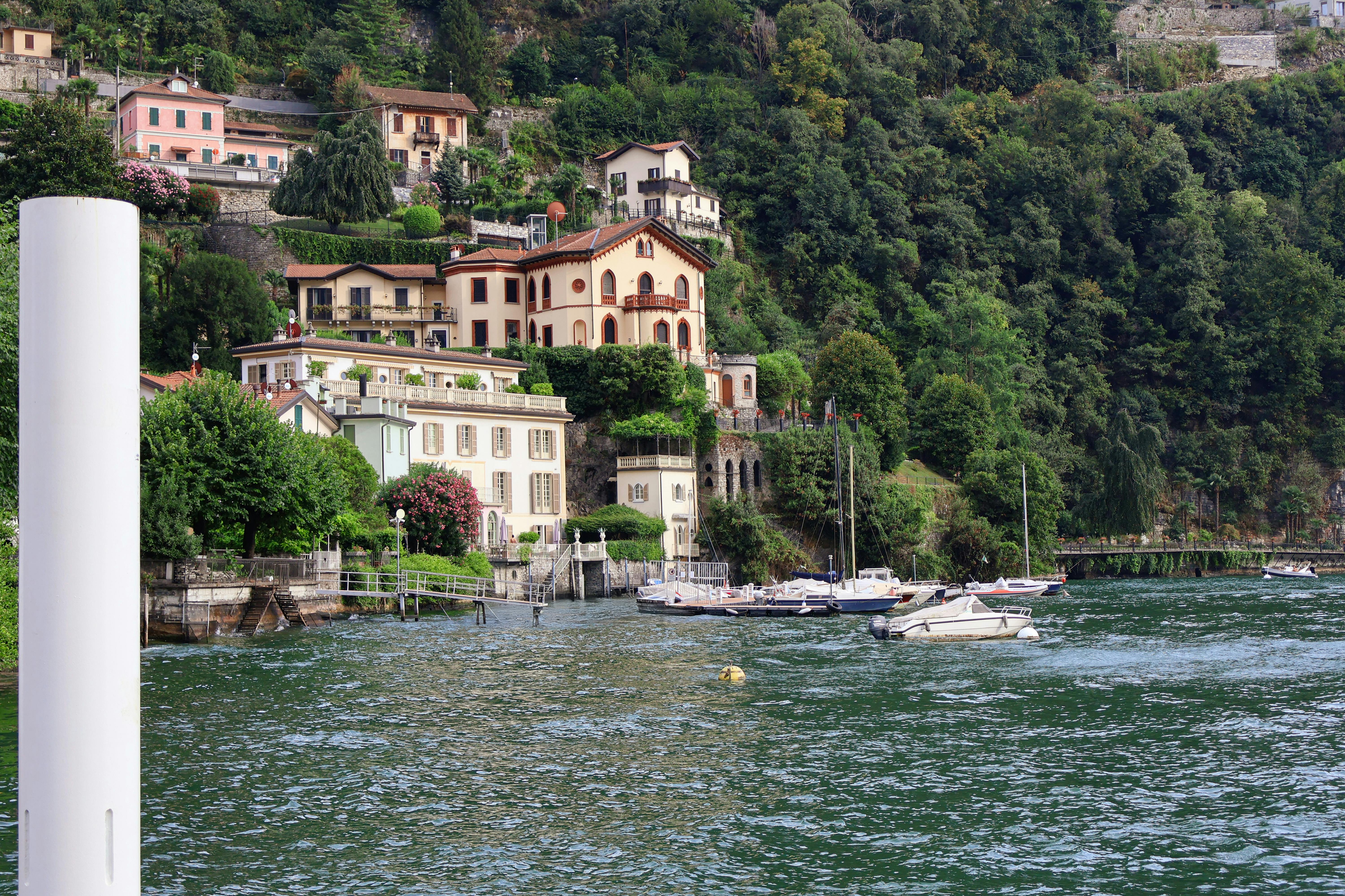 Free Charming villas by Lake Como surrounded by lush greenery and boats on a peaceful summer day. Stock Photo