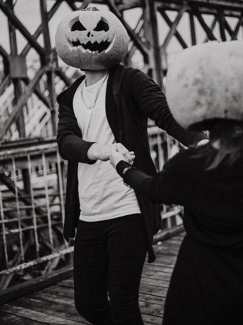 Free A whimsical black and white photograph of two people with pumpkin heads dancing on a bridge. Stock Photo