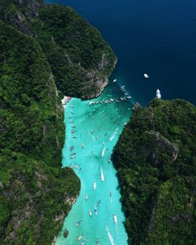 A stunning aerial view of a turquoise lagoon in Thailand filled with boats and surrounded by lush cliffs.