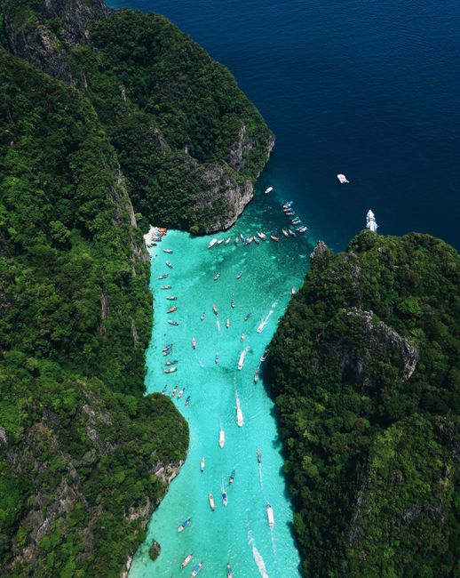 A stunning aerial view of a turquoise lagoon in Thailand filled with boats and surrounded by lush cliffs.