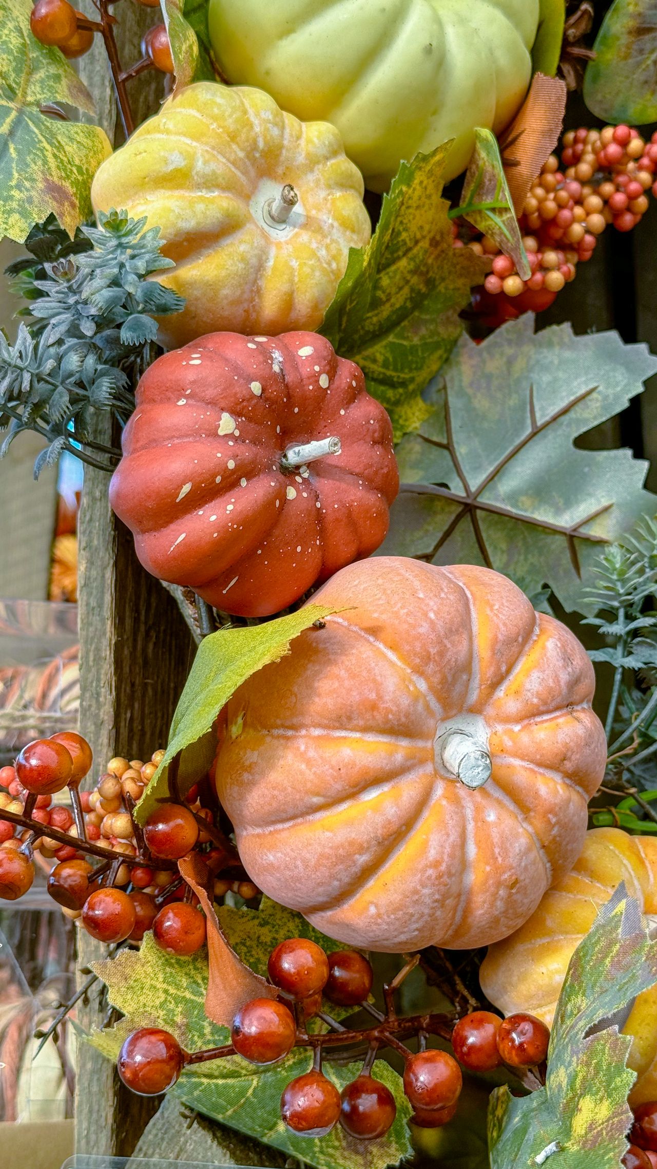 Cluster of decorative pumpkins in orange, red, and green with berries and fall leaves