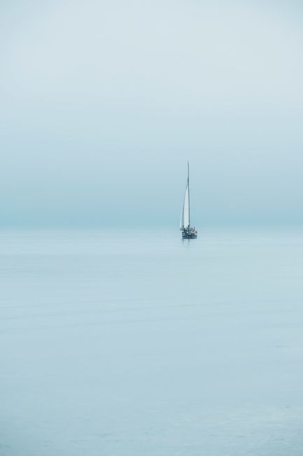 A serene scene of a lone sailboat on the calm waters of Lake Constance, enveloped in mist.