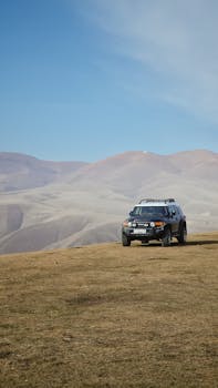 A lone SUV parked on a grassy hill with distant barren mountains under a clear blue sky.