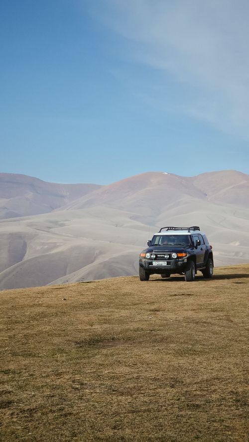 Free A lone SUV parked on a grassy hill with distant barren mountains under a clear blue sky. Stock Photo