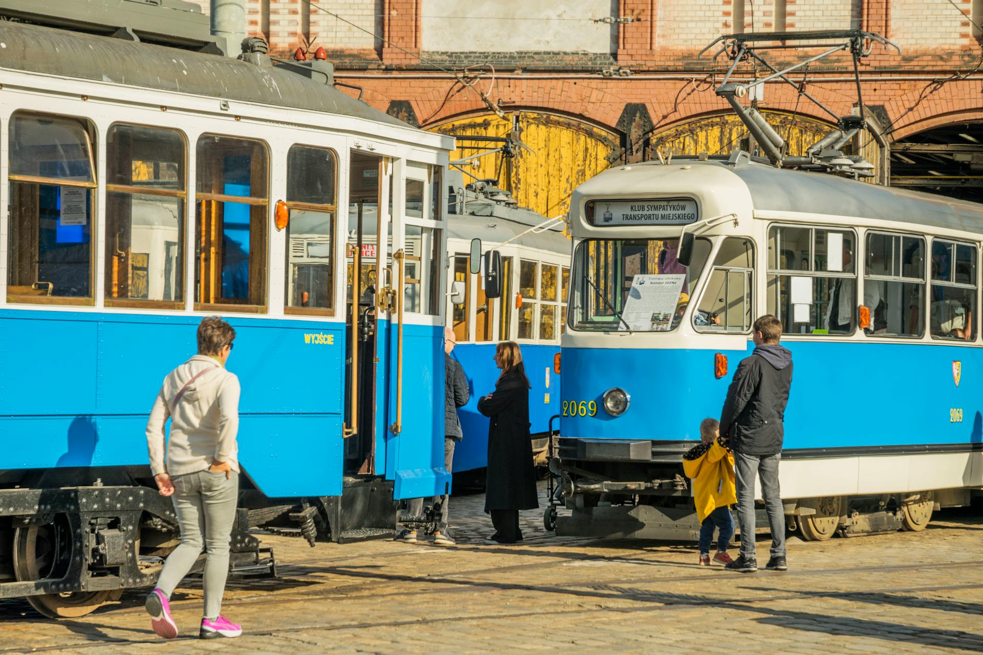 A vibrant scene of historic trams with people outside a depot in Wrocław, Poland.