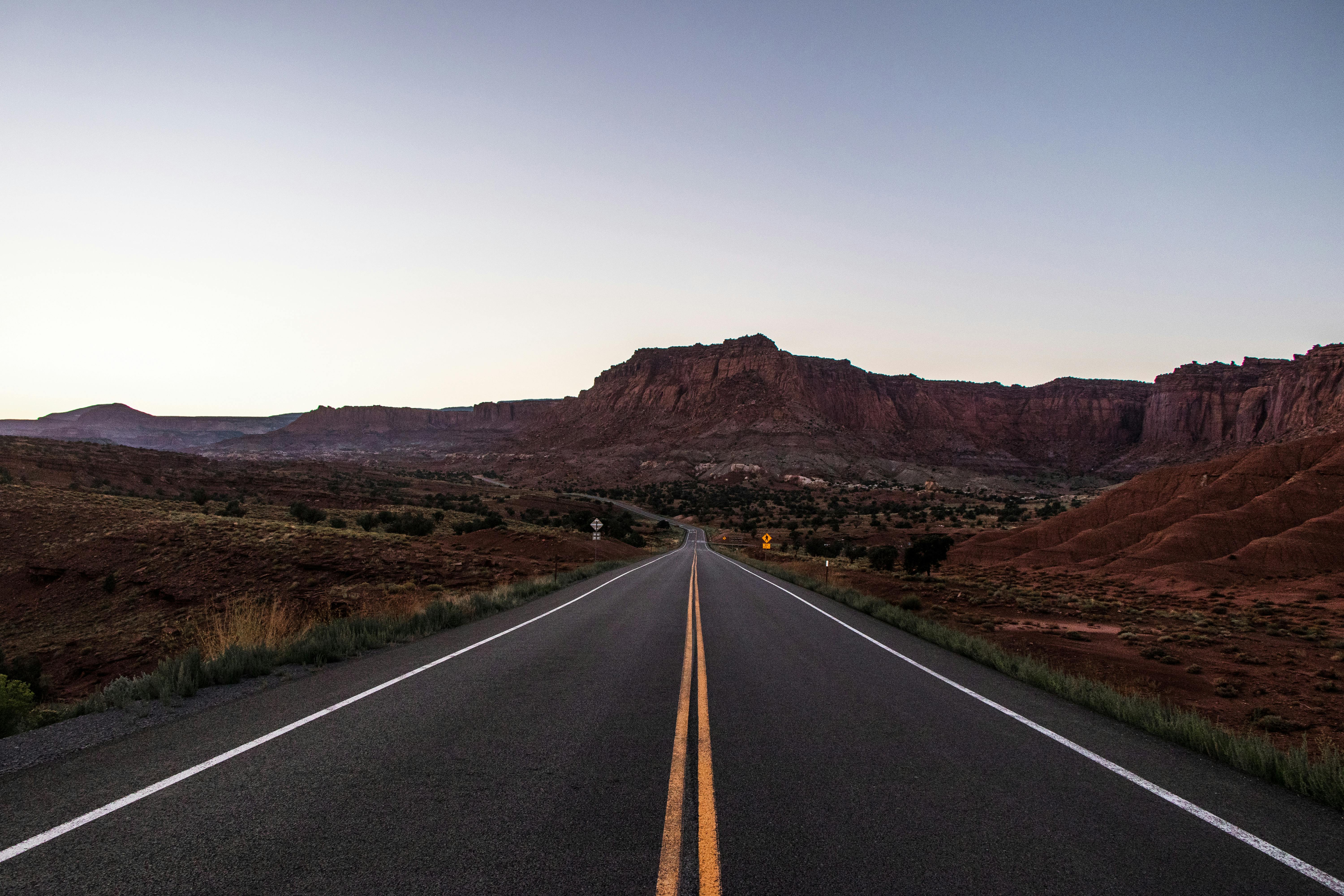 Empty highway leading through Utah's stunning desert landscape at sunrise.
