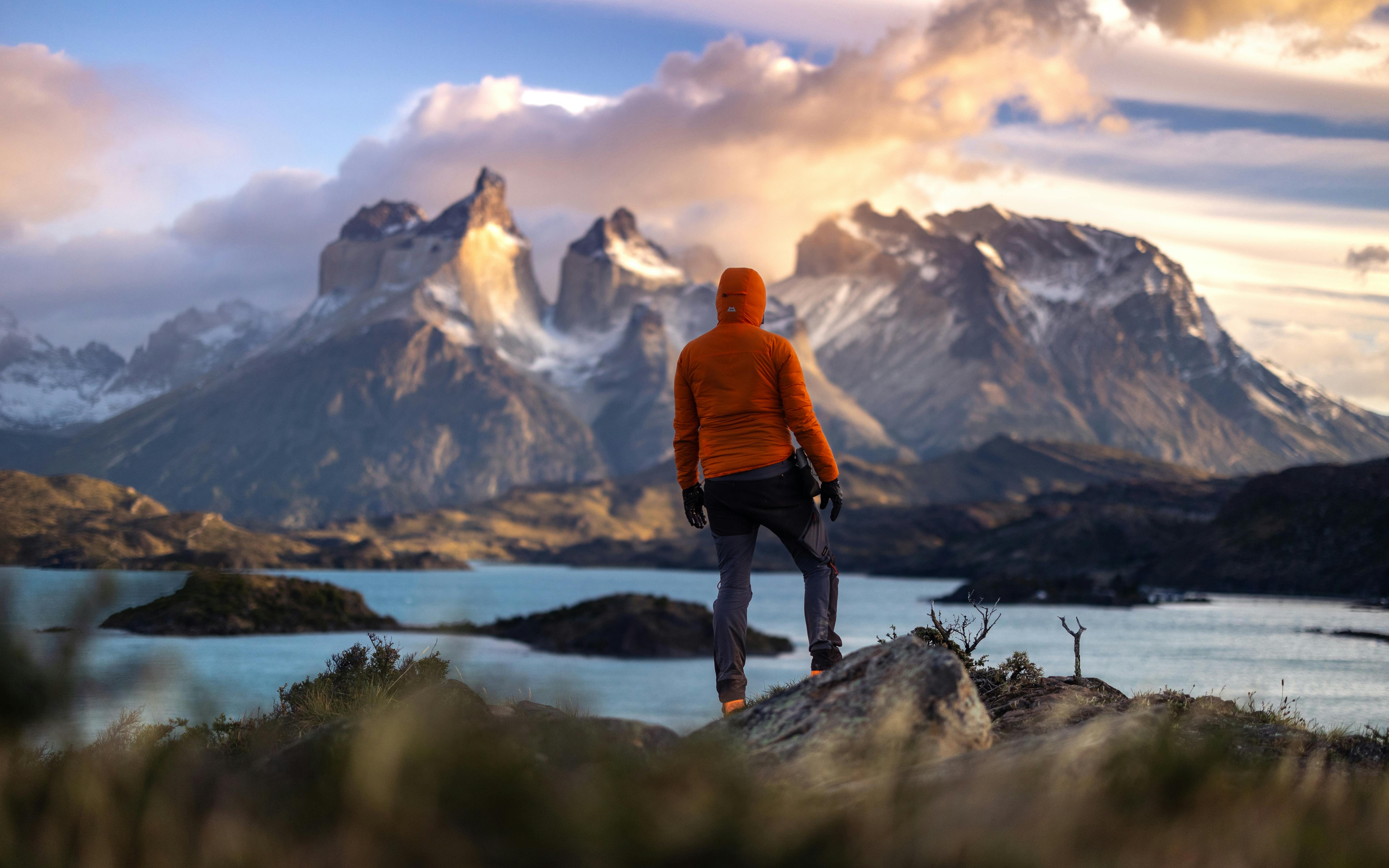 A hiker stands at sunrise in Torres del Paine, Chile, overlooking majestic mountains and a tranquil lake.
