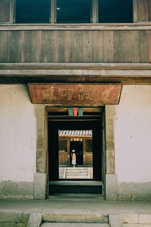 Free A woman stands inside a traditional Chinese wooden building, viewed through open doors. Stock Photo