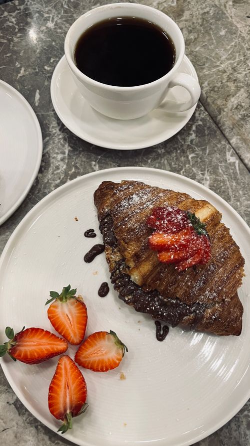 Free Flaky croissant topped with strawberries served with a cup of coffee on marble table. Stock Photo