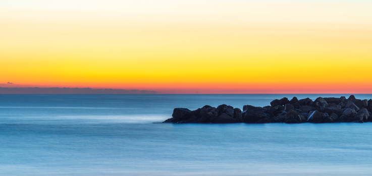 Tranquil sunrise over rocky outcrop in Comunidad Valenciana, Spain, with vibrant colors.