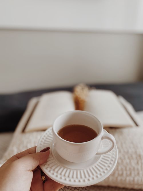 Free A close-up of a tea cup in hand with an open book in the background, creating a cozy setting. Stock Photo