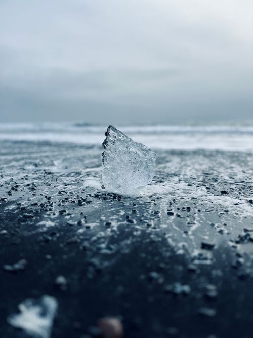 Free A close-up of an ice chunk on a black sand beach in Iceland with a misty backdrop. Stock Photo