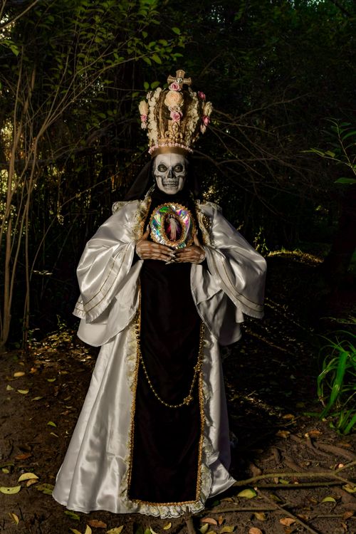 Free A person dressed as a skeleton with a floral headdress and robe in a forest environment, capturing a mysterious vibe. Stock Photo