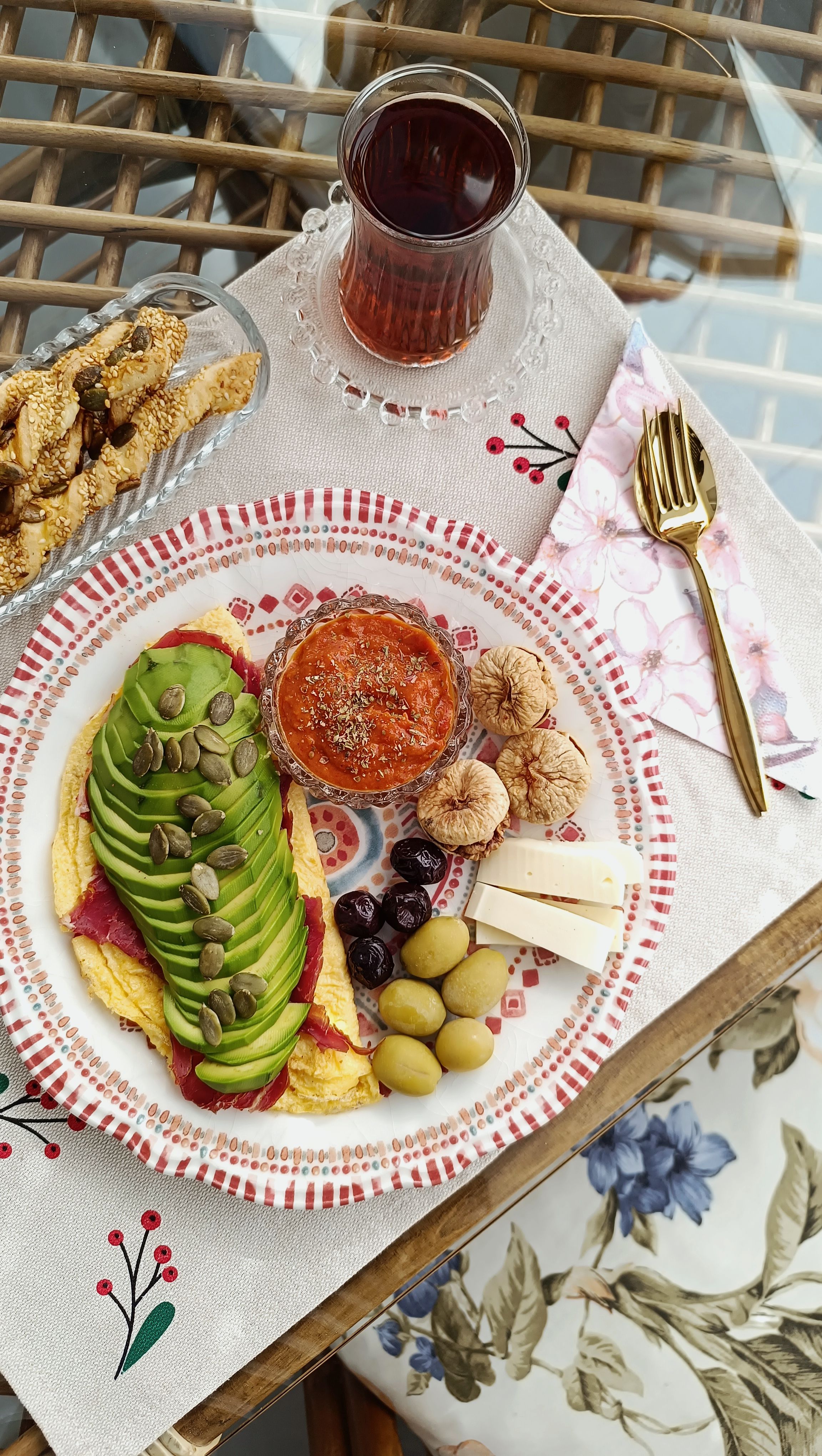 A vibrant brunch setup with avocado omelette, olives, figs, tea, and more on a decorative table.
