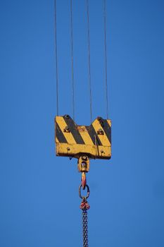 Close-up of a construction crane hook suspended in clear blue sky, symbolizing industry.