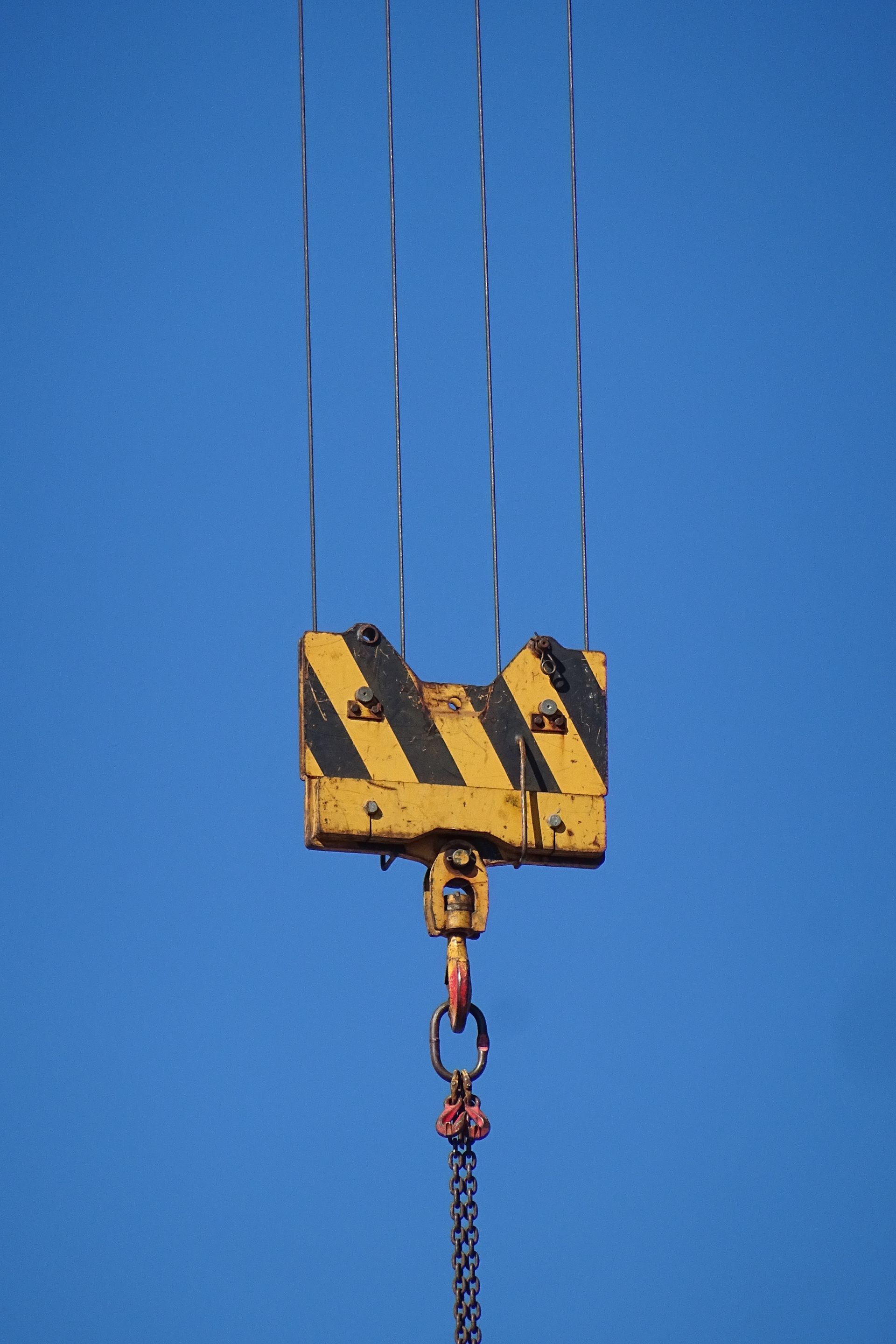 Industrial crane hook suspended against a clear blue sky
