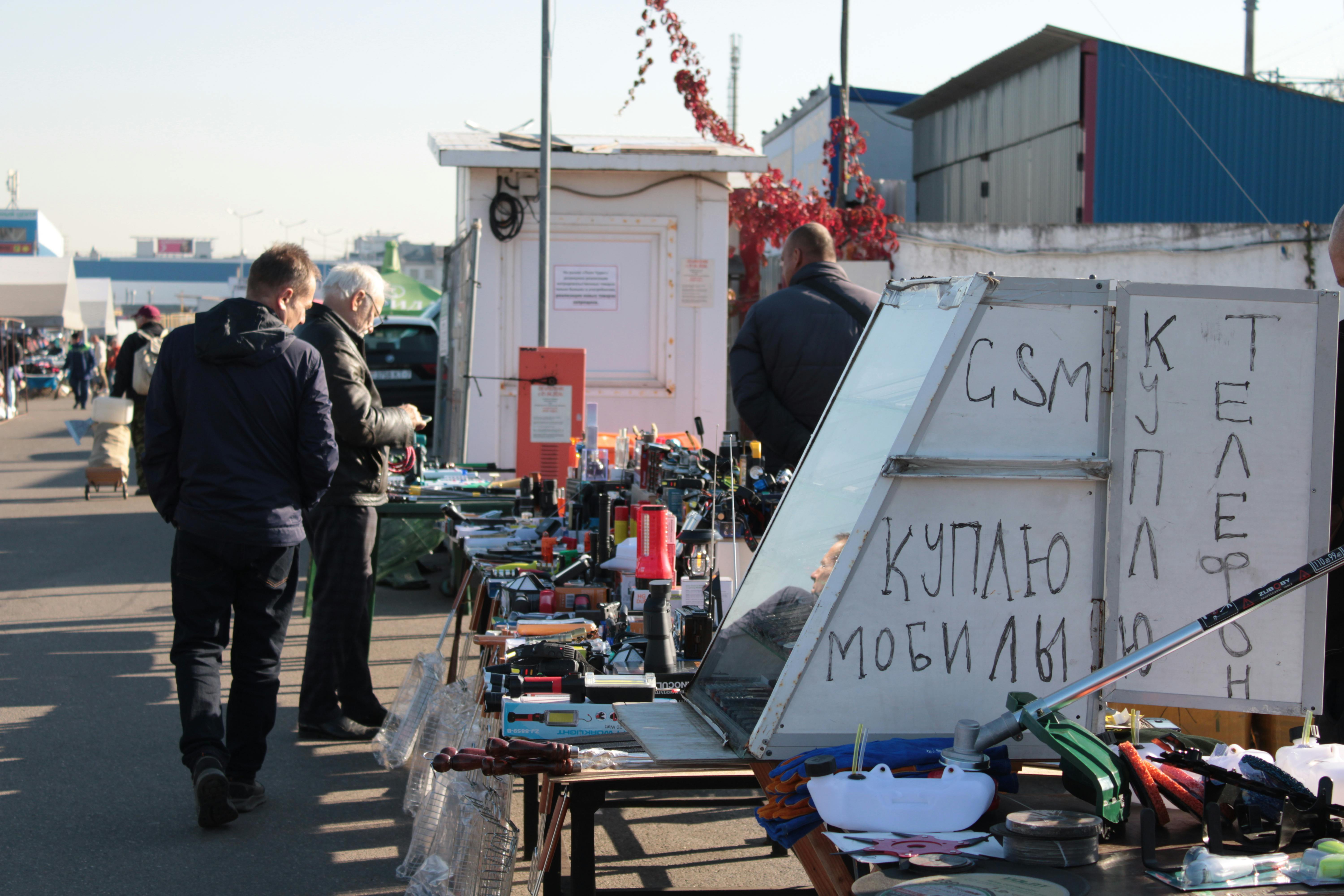 People browsing electronics at an outdoor market with various gadgets on display.