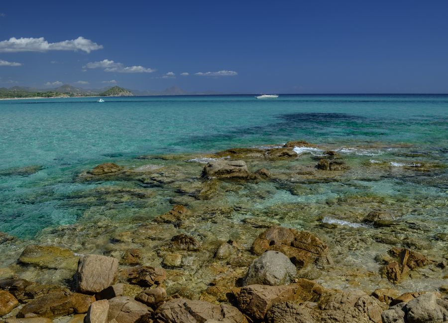 Stunning clear turquoise waters and rocky shores of a Sardinian beach under a bright blue sky.