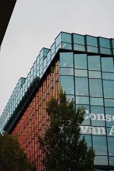 Contemporary architecture featuring a glass facade with tree in foreground, daylight.