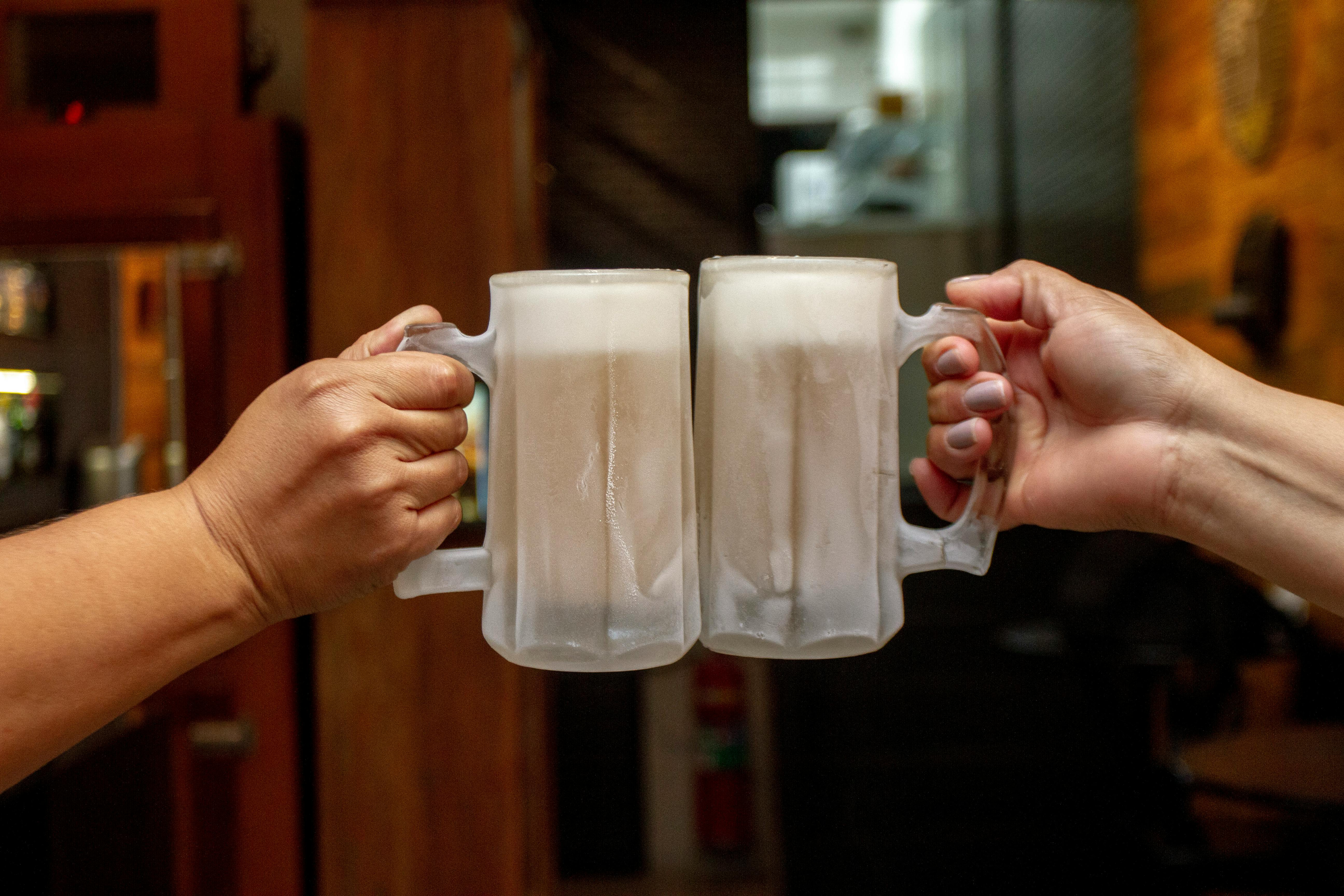 Two people clinking frosty beer mugs indoors, celebrating in a cozy Brazilian bar.