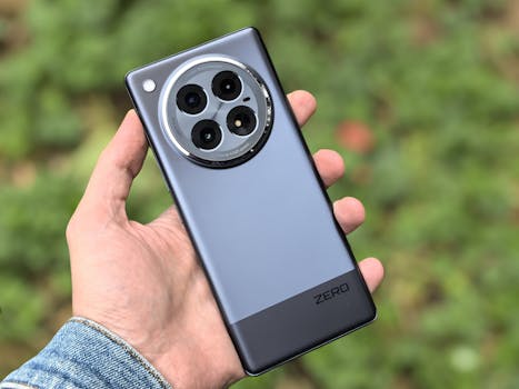 Hand holding a sleek smartphone with a triple camera and shiny silver design.