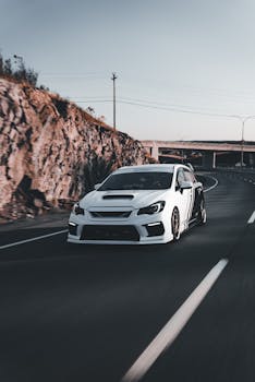 A high-performance white sports car speeds down a scenic mountain highway, showcasing sleek design and power.