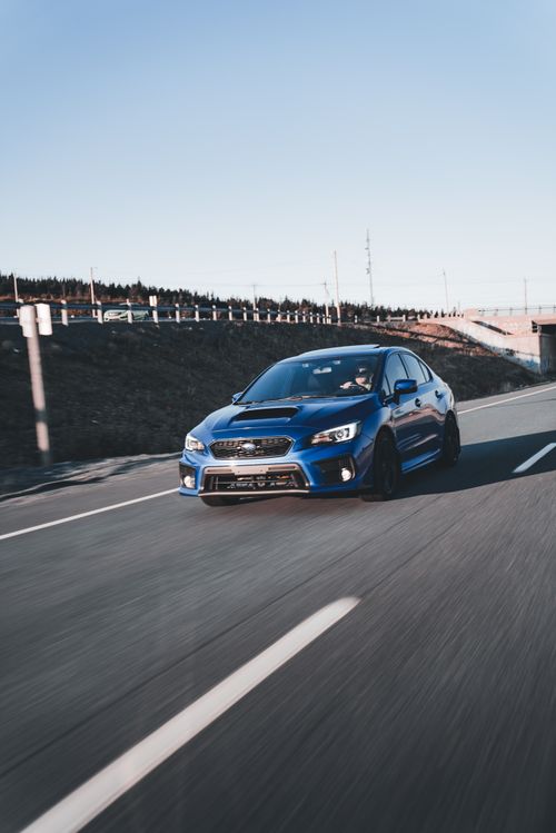 Free A sleek blue sports car speeds on a deserted highway at sunset, capturing the thrill of the open road. Stock Photo